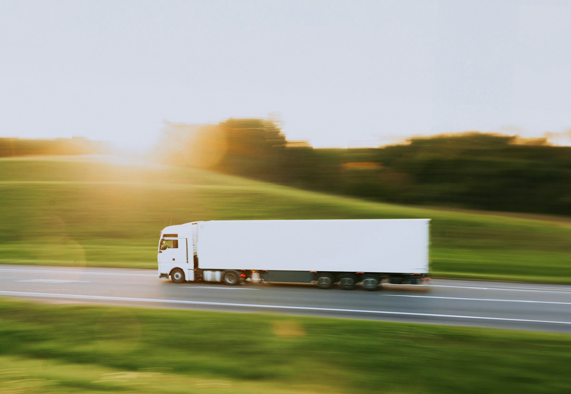 White semi truck driving along a highway past green fields