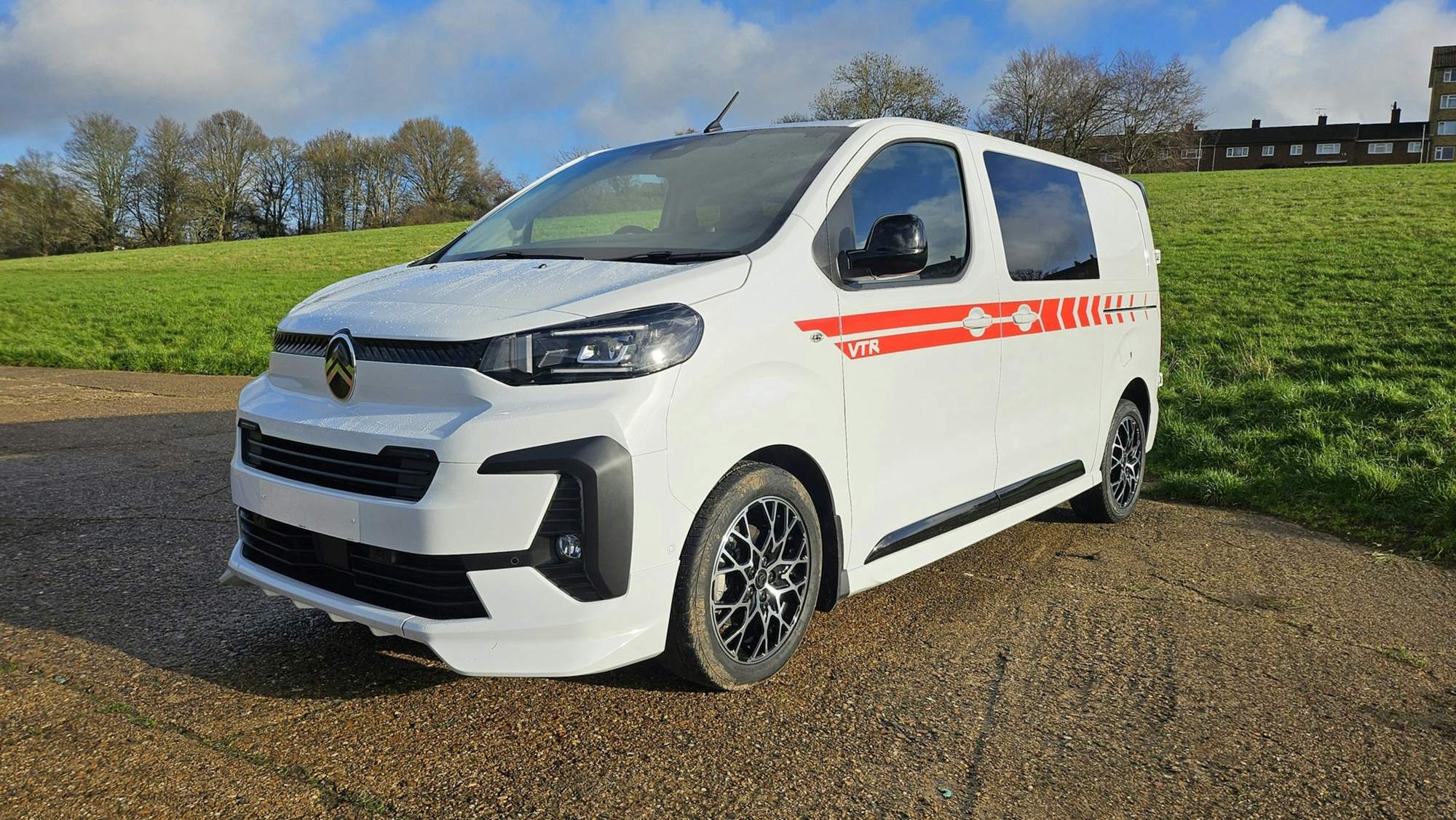 White van with red stripe graphics parked on a gravel lot beside green grass